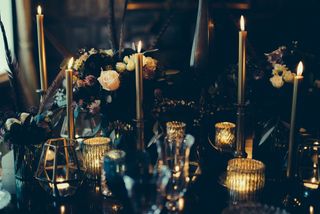 A dark themed Halloween tablecape with gold candles, black flowers and feathers