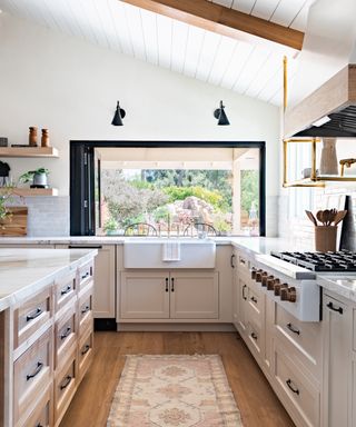 kitchen with pale pink cabinetry, black window frame, large sink, black wall lights vaulted shiplap ceiling, open shelving, kitchen island