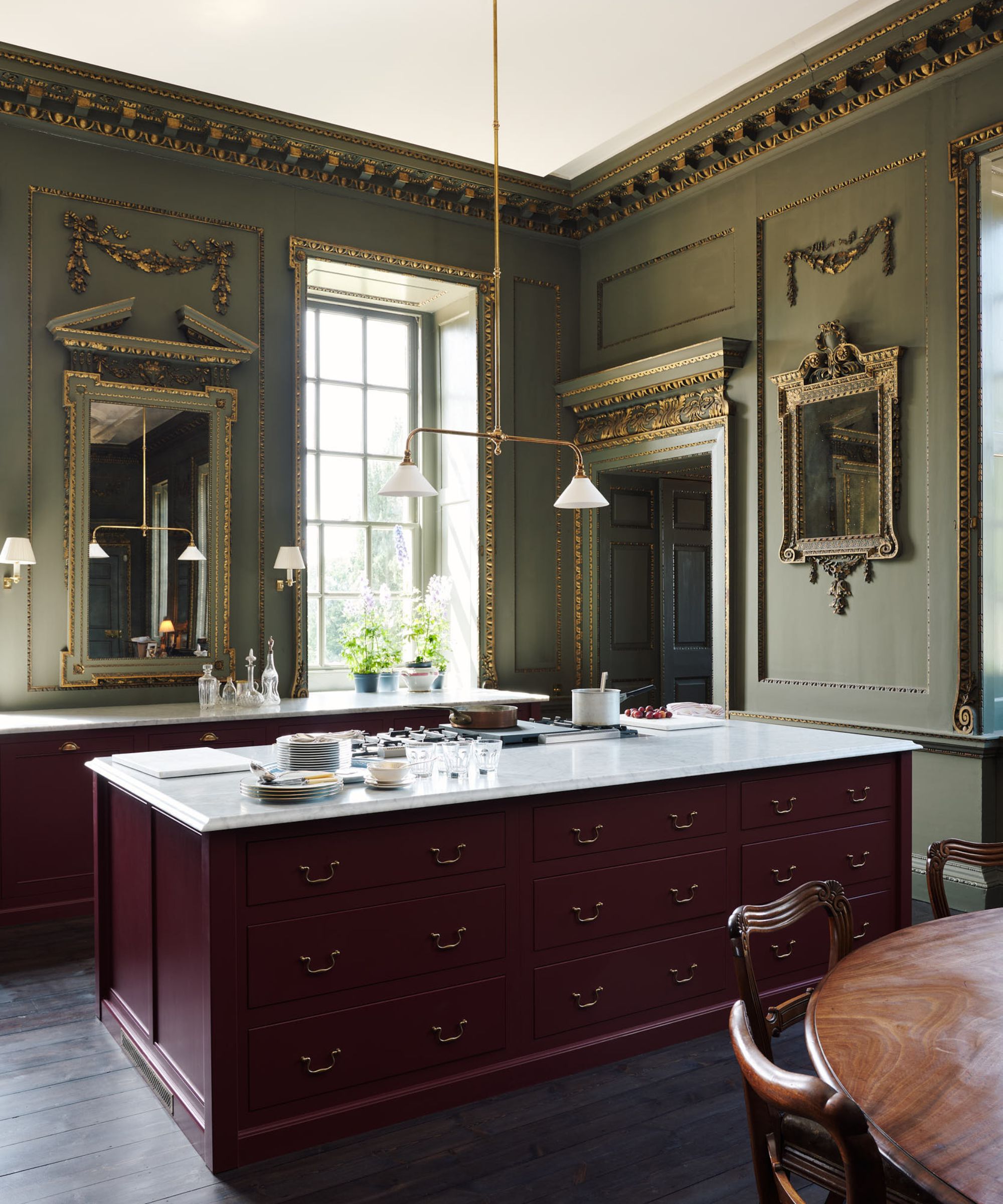 A stately home kitchen with green walls, red cabinets, ornate mirrors, and marble countertops