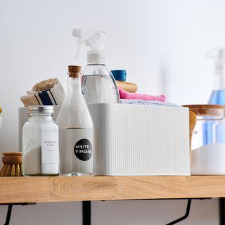 Shelf lined with cleaning products, some stored in a white enamel cleaning caddy
