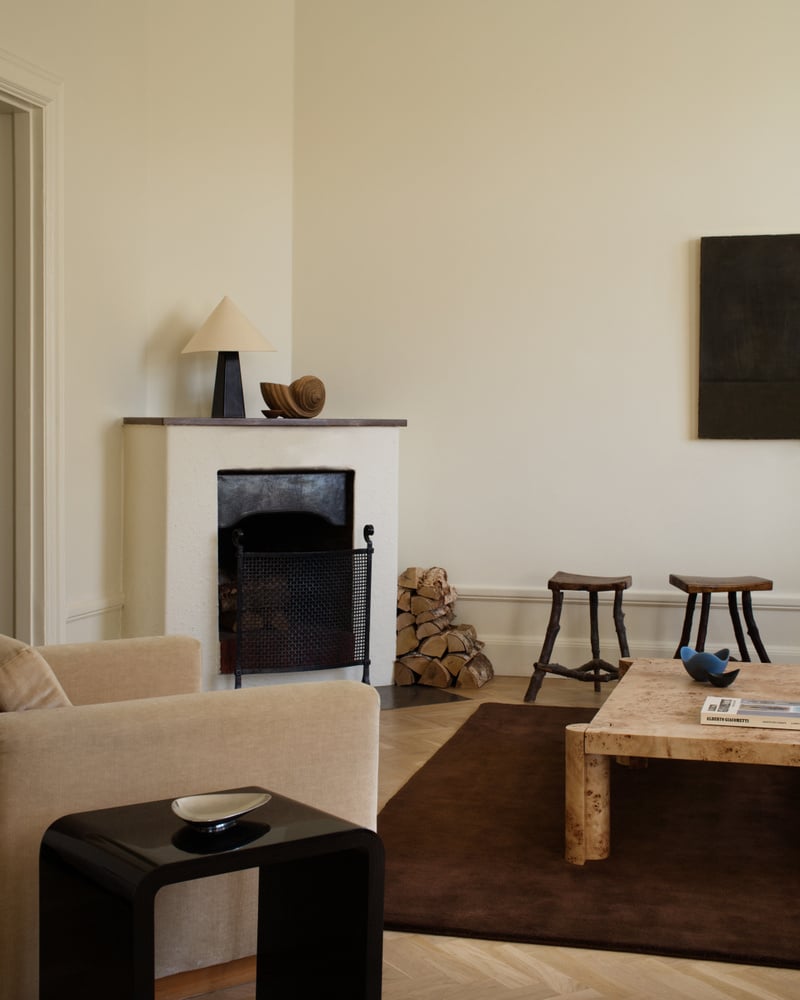 Image of a dark brown rug in a modern, neutral living room. There is a beige, velvet accent chair and a burl wood coffee table. A fire place is in the corner.