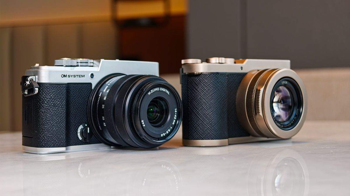 OM System PEN vs Panasonic Lumix L10: two micro four thirds cameras side by side on a white marble surface with lamp light in the background