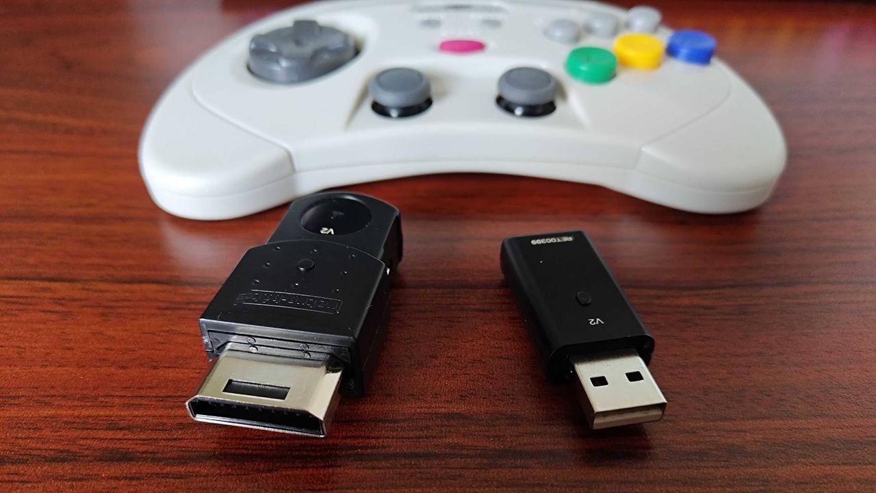 Retro-bit Sega Saturn Pro controller dongles in front of gamepad on woodgrain desk.