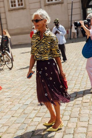 Woman at fashion week wearing preppy outfit featuring a tiger print collared shirt, Prada fringe skirt, and yellow kitten heels