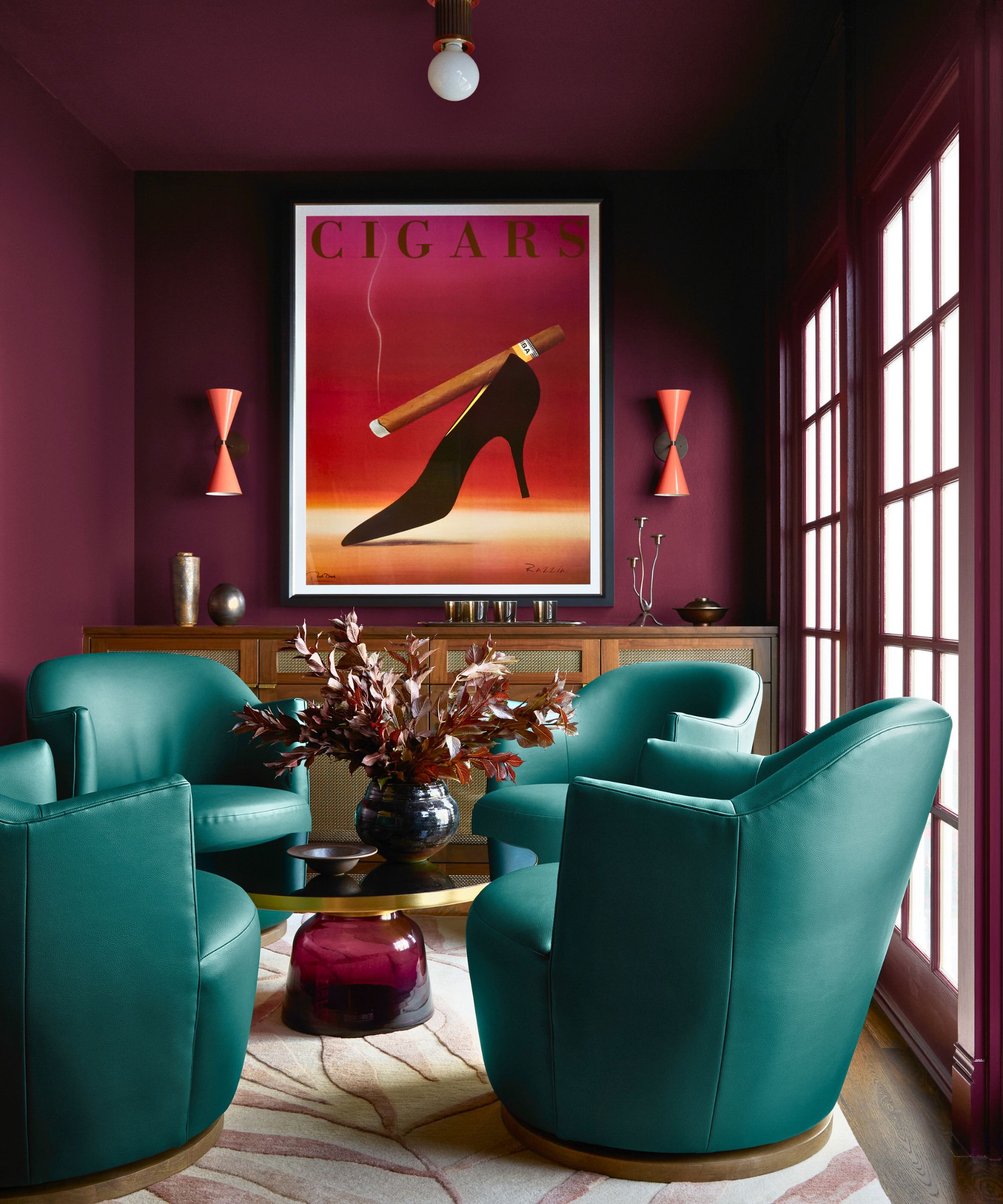 snug with dark red walls, teal green chairs, a built in wooden console and large artwork