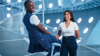 Ncuti Gatwa and Varada Sethu stand smiling in FIfteen's TARDIS for a Doctor Who Season 2 promo shoot.