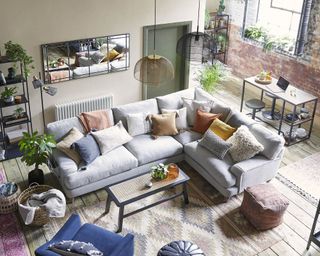 An industrial boho living room with grey L-shaped sofa and exposed brick wall