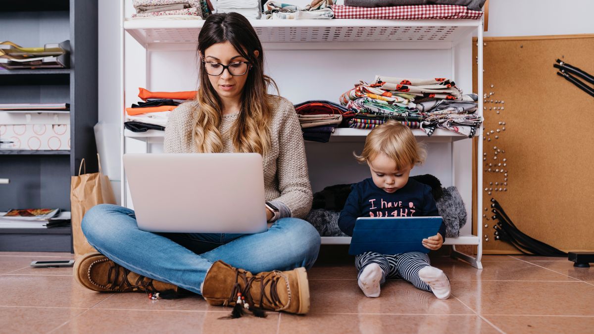 Mother and young daughter sitting on the floor at home using a laptop and tablet