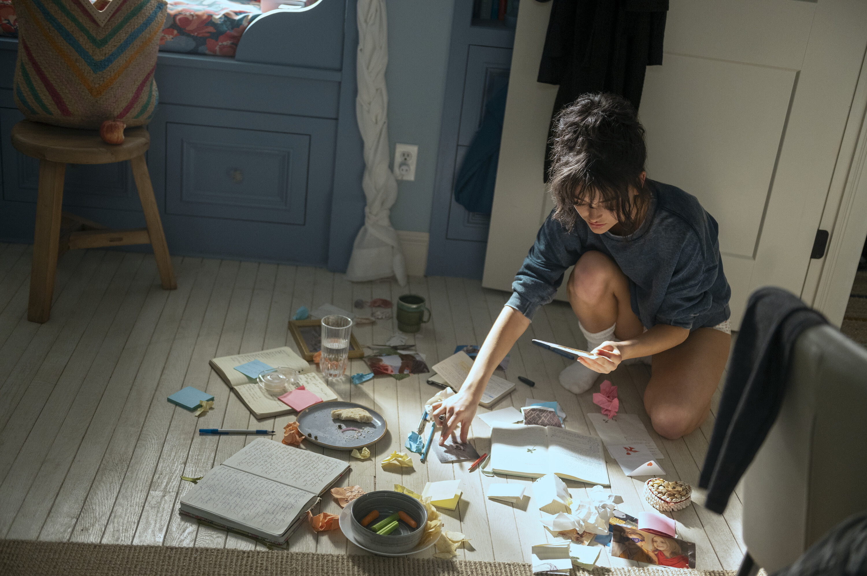 A teenage girl kneels on the floor and searches through a pile of notebooks, papers, and notes, in 'We Were Liars.'