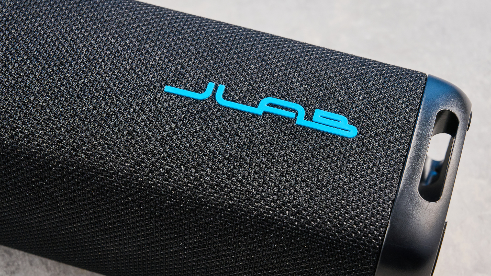 the jlab jbuds party speaker with LED rainbow lights photographed against a blue background