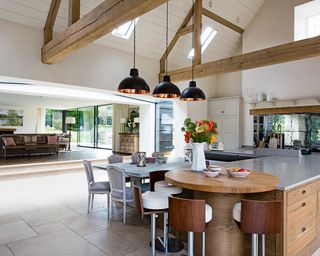 An example of kitchen extension ideas showing a large kitchen with wooden beams and a wooden, circular island attachment with bar stools in front of a dining table