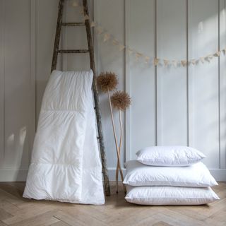Wood-panelled wall with a ladder displaying a duvet and pillows stacked next to it
