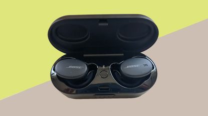Bose Sport Earbuds review: the buds in their charging case against a green and beige background