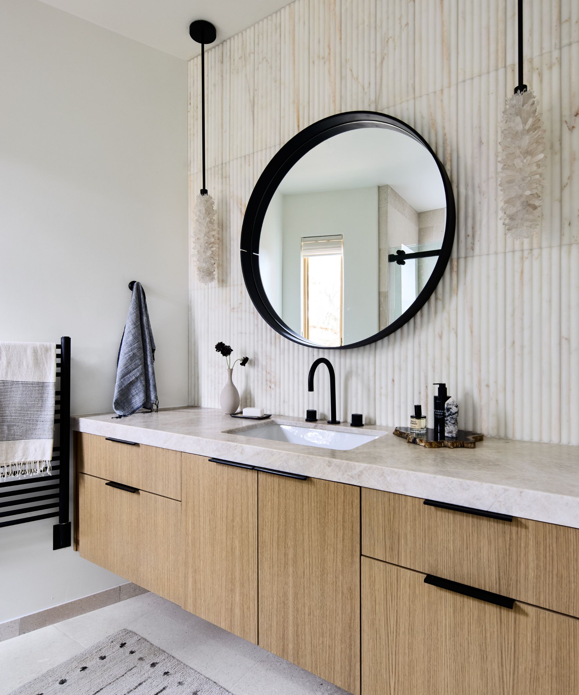 Modern bathroom with wood and marble vanity, round black mirror and two crystal lights hang above