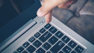 A close up of a person's hand hovering over the delete button on a silver-coloured laptop