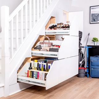 three large pull out drawers underneath a white staircase, the drawers containing books, wine, bags and shoes