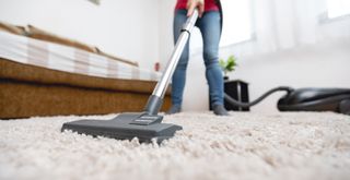 Person vacuuming a living room rug to show how to reduce dust