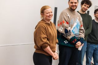 sarah snook wearing a brown sweatshirt smiling surrounding by crew at the first rehearsal for the picture of dorian gray on broadway