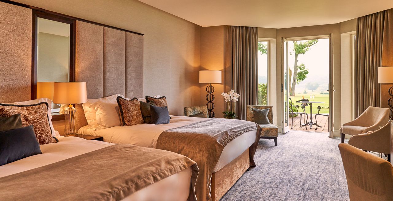 A hotel room with two beds and the doors open to a patio