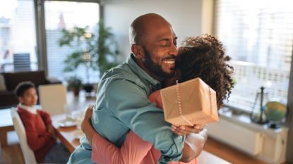 Happy teenage girl embracing her dad at home, giving him a father's day gift and celebrating together.