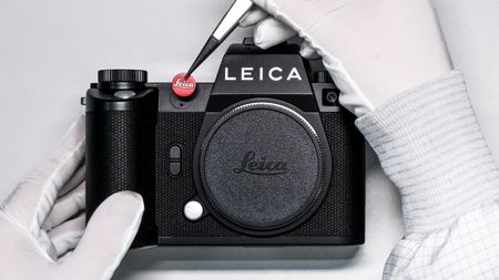 Gloved hands putting the Leica red dot logo on the front of an SL3 camera