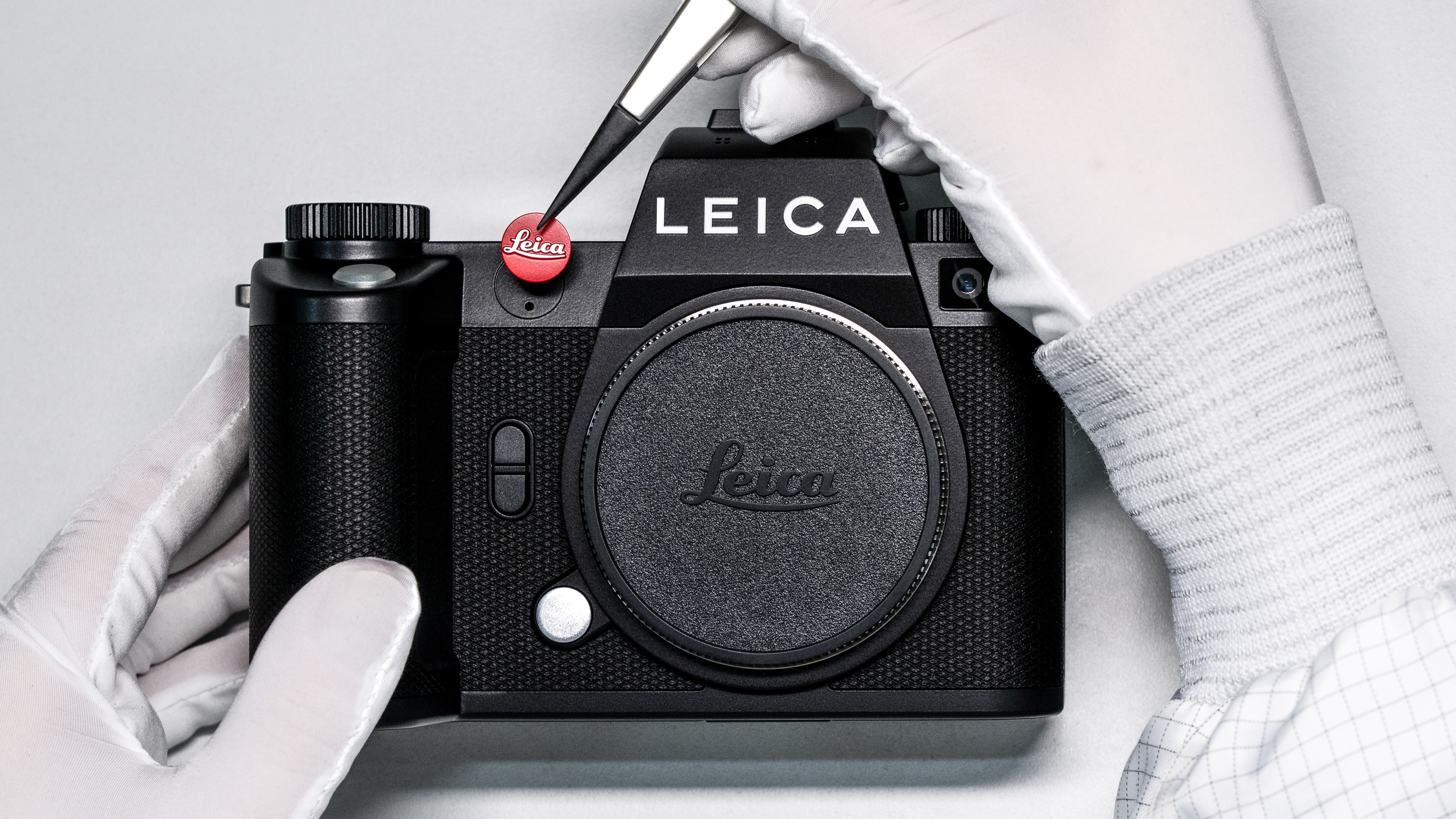 Gloved hands putting the Leica red dot logo on the front of an SL3 camera