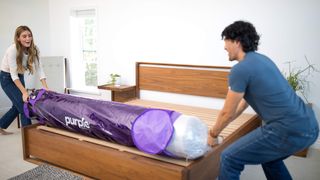A man and a woman remove a Purple mattress from its packaging before it starts to expand, ready for sleeping on later