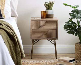 Dunelm Priya Side Table made from mango wood by the side of a bed with rug on the floor and plant and candle on top