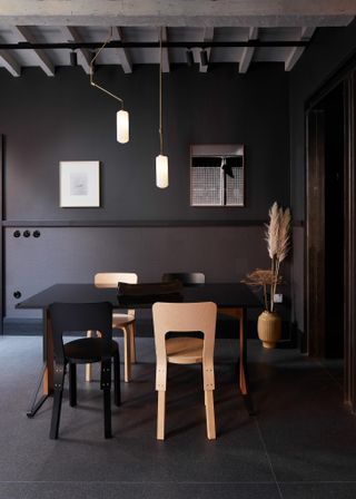 A dark grey dinning area with a wooden table and chairs, wall paintings and a potted plant.