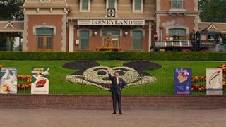 Mr. Banks, played by Tom Hanks, stands at the gates of Disneyland in front of a Mickey Mouse garden in Saving Mr. Banks
