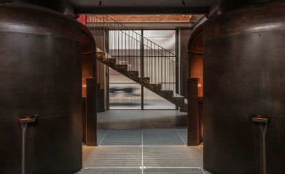 Stone staircase going down into basement with large boilers and grey metal flooring