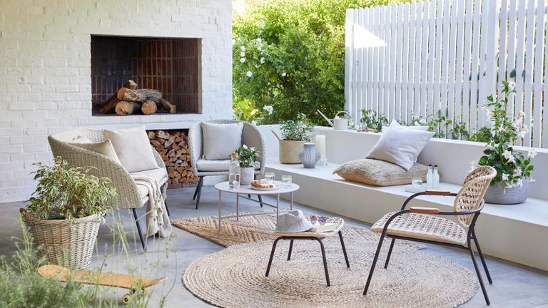 A neutral Scandinavian-inspired outoor living space with 4-piece lounge set, open weave garden chair and footstool, Jute round rug, carafe with cork, floor cushion, natural seagrass basket and wicker log basket