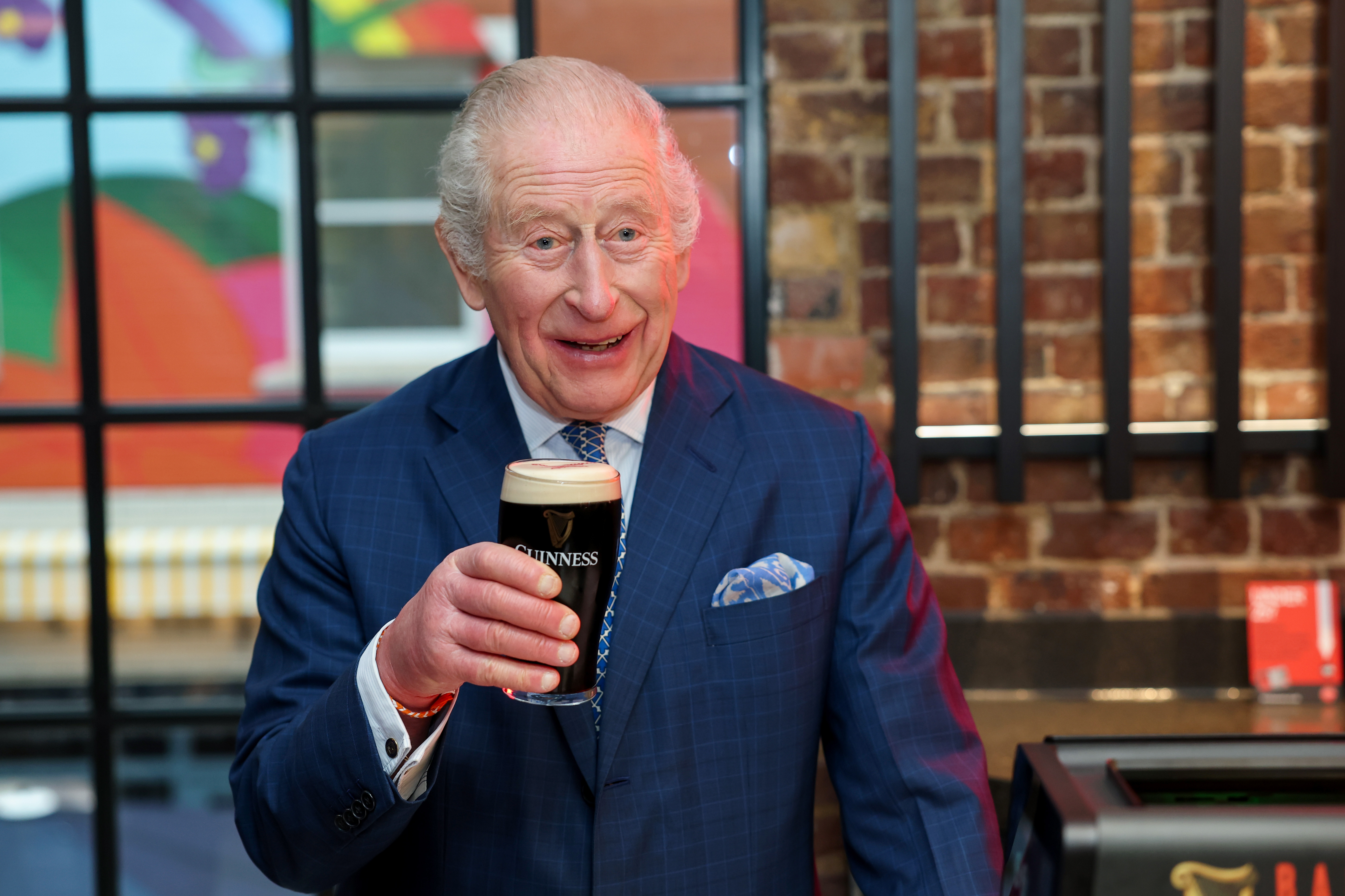King Charles smiling holding up a pint of Guinness