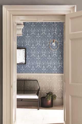 Patterned wallpaper above and below dado in hall with bench and plant