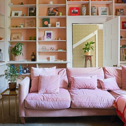 Living room with built in shelving and decorative furnishings, large pink L-shaped sofa