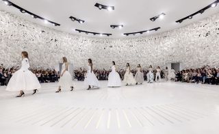 Images of models walking on to the white circular stadium like set in a line in big white dresses
