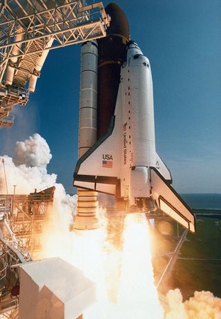 a space shuttle with fuel tank and side solid rocket boosters ignited launches during a clear day.