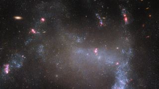 A wispy collection of stars, bright pink gas clouds and dust in an irregular galaxy in deep space.