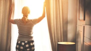 Woman closing the curtains to the daylight wearing pyjamas
