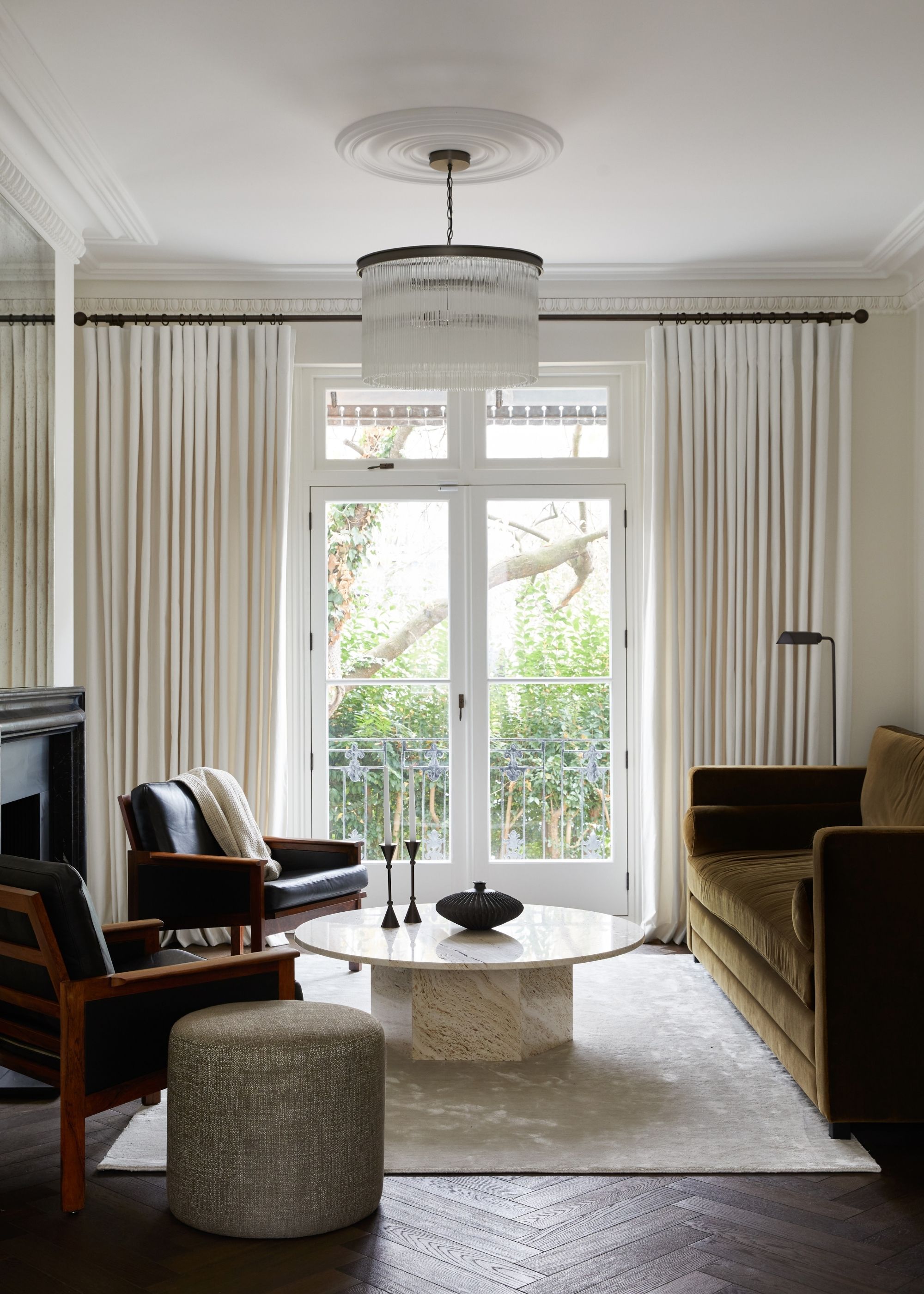An elegant living room in a traditional home with tall, warm white walls and ceiling, warm white curtains in front of the French doors, and an olive green velvet sofa.