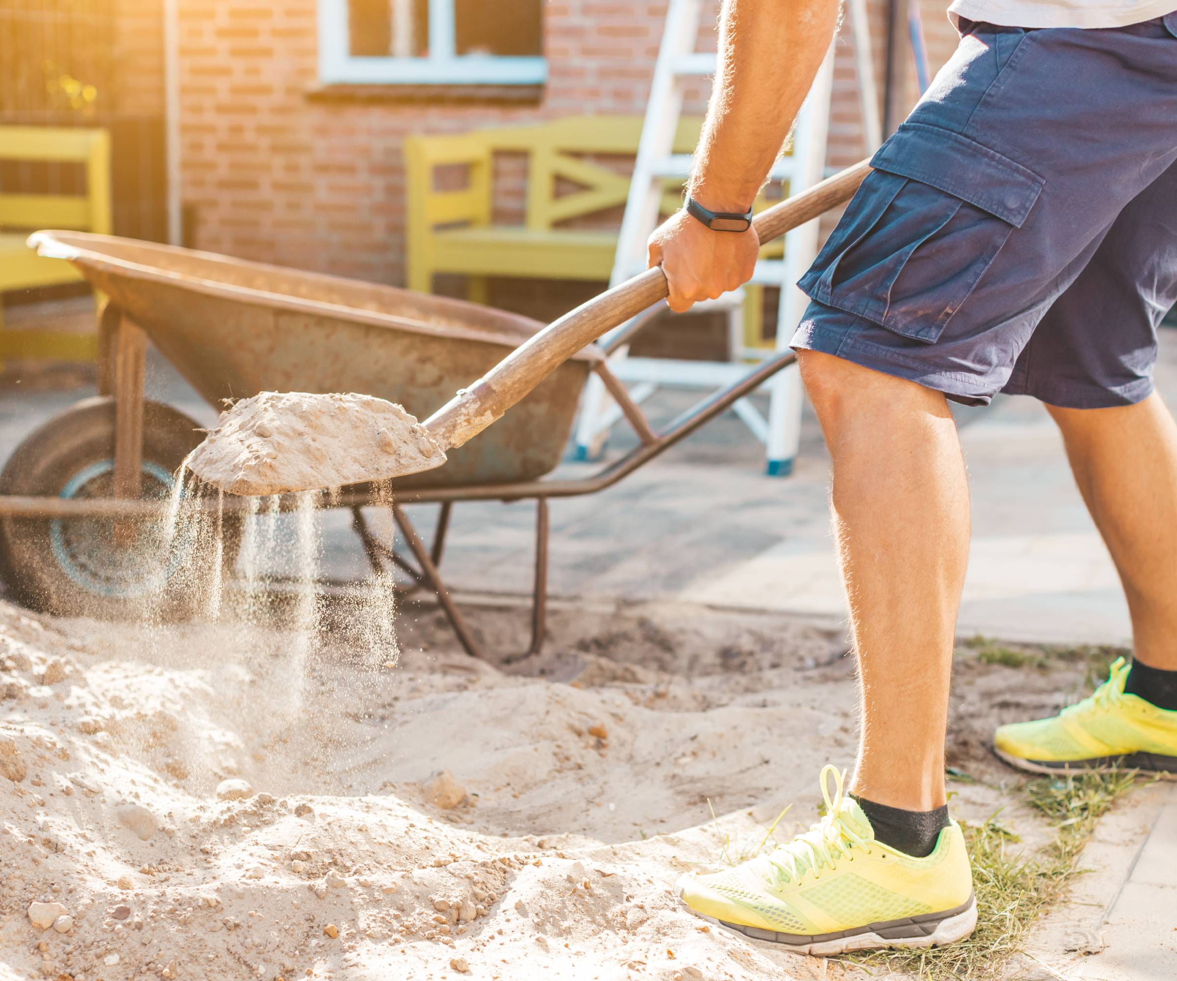 A man shovels sand next to a wheelbarrow