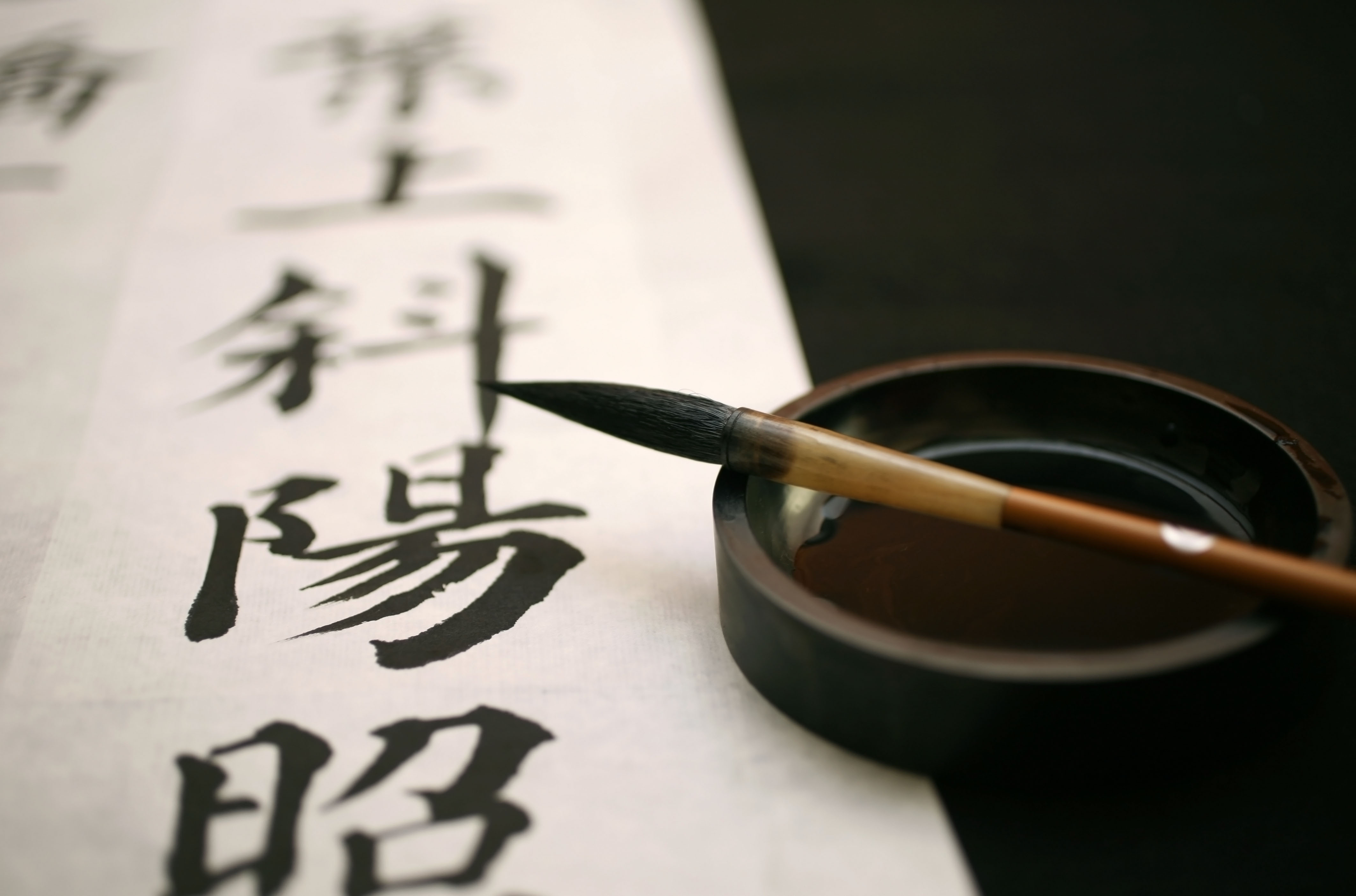 A piece of rice paper with black calligraphy characters on it next to an inkwell and brush