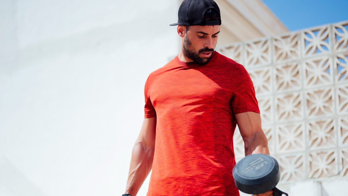 Man holding two dumbbells looking down at the weight, outdoors