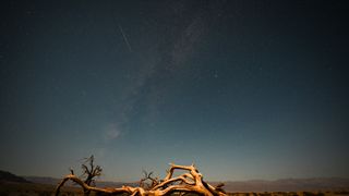 a meteor streaks through the sky above the desert