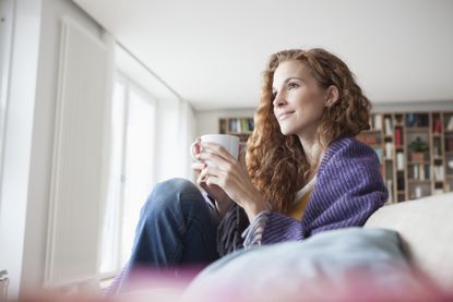 Woman at home sitting on sofa holding mug