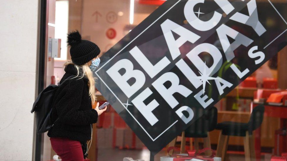 A woman in front of a shop window displaying a Black Friday deals sign