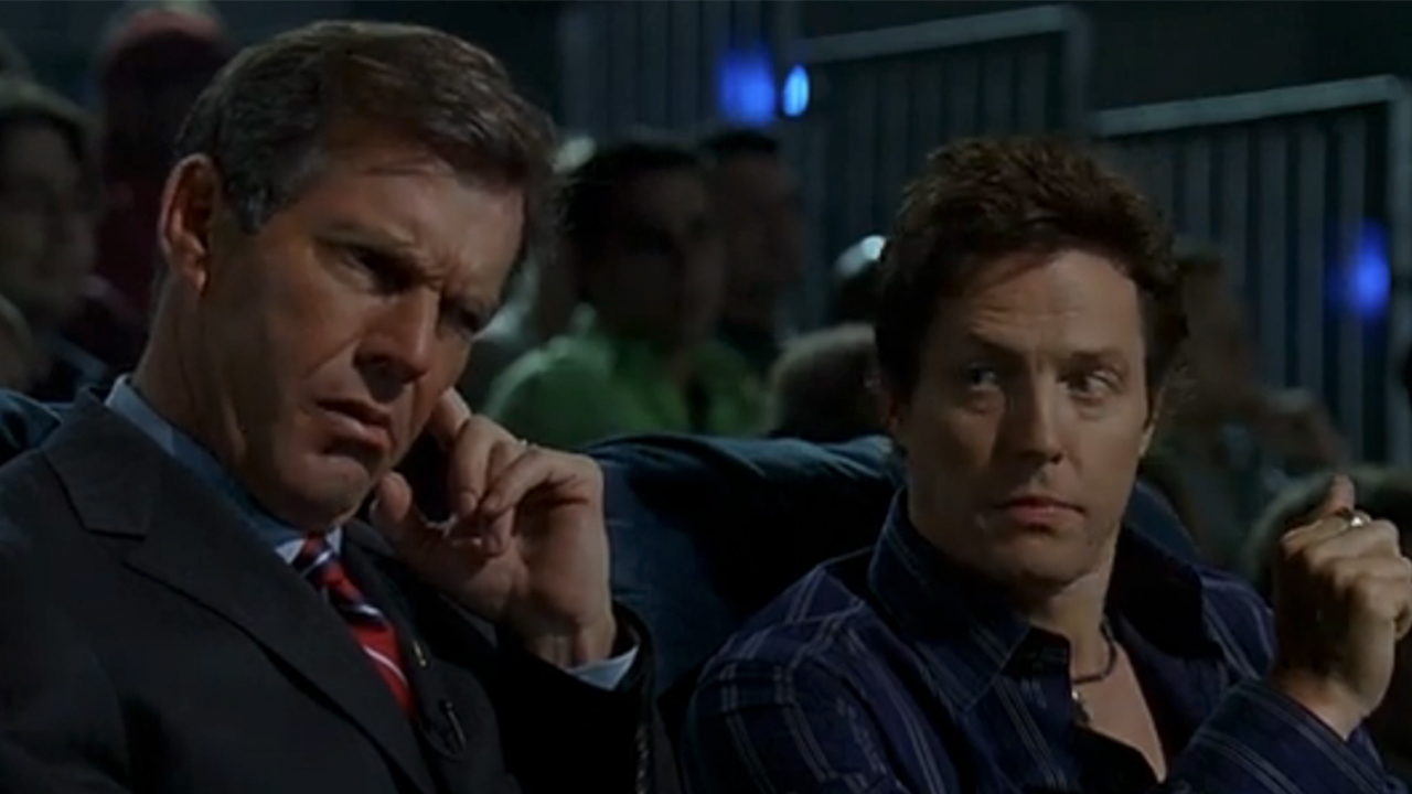 『American Dreamz』でヒュー・グラントが彼を見守る間、スーツを着て耳を押さえるデニス・クエイド