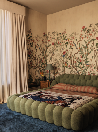 A bedroom with a cream wallpaperm a green tufted bed and blue carpet