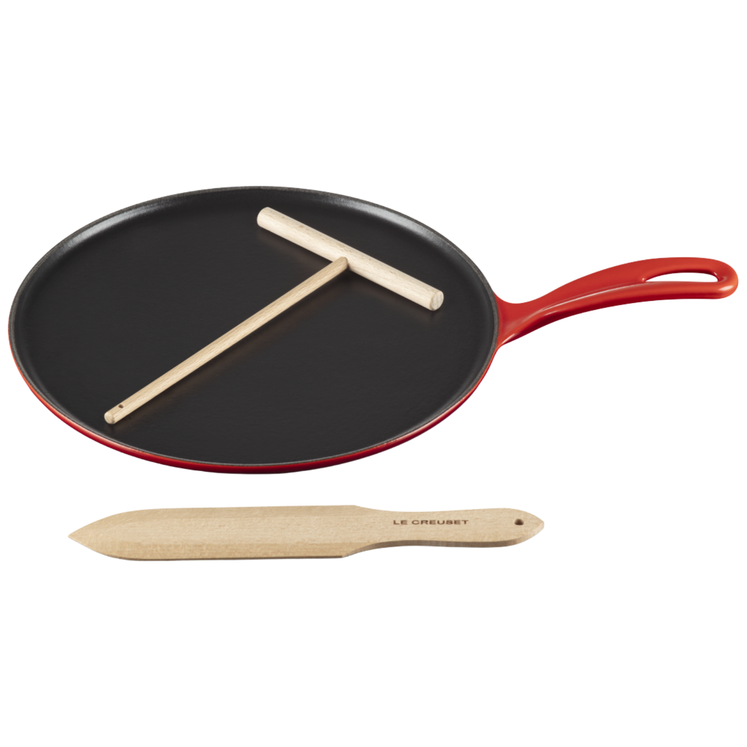 A small cast iron crepe pan with a red exterior alongside a wooden tool for flipping and spreading the batter by Le Creuset