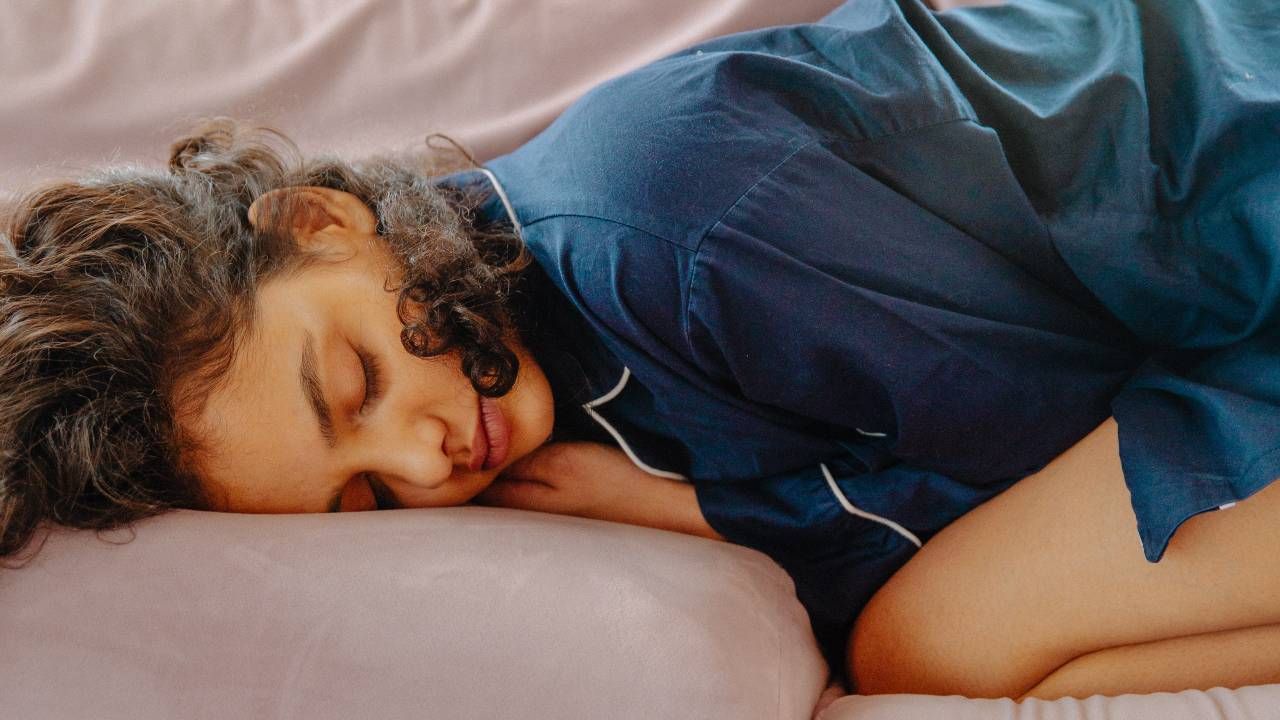 Woman in blue silk pyjamas napping curled up on a pink sofa